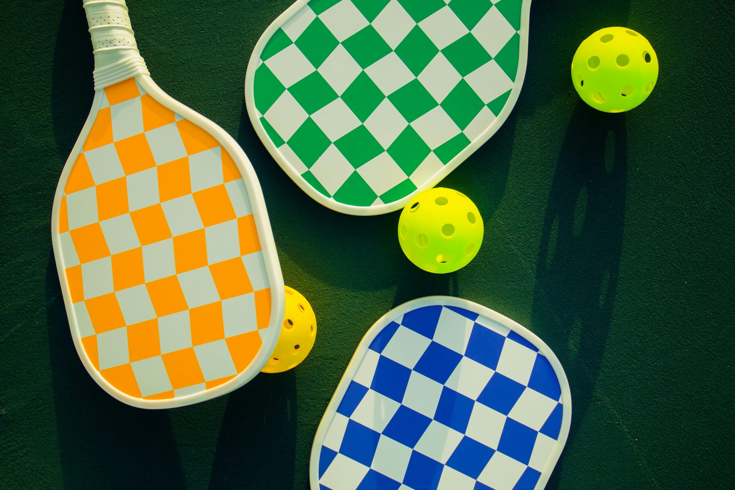 Vibrant pickleball paddles and balls arranged on a sunny sports court.