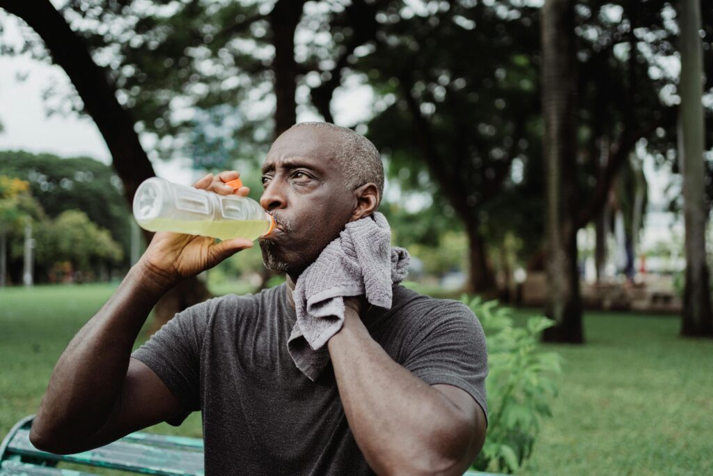 Adult man drinking sports beverage and wiping sweat in a park.