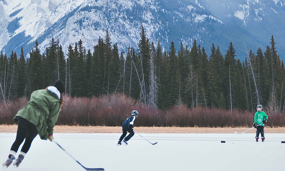 a woman and two kids play hockey on iced pond